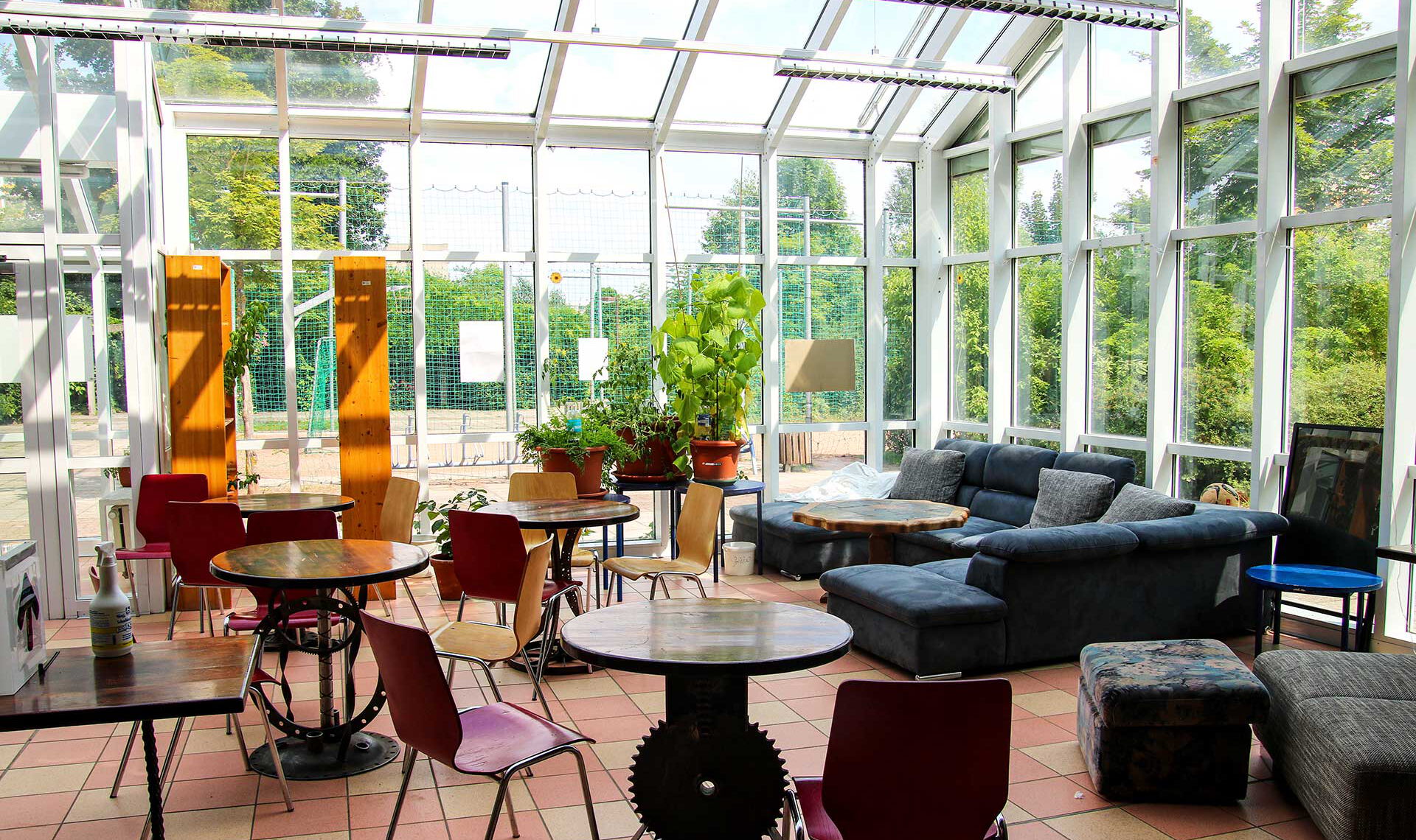Der Sitzbereich im Erdgeschoss mit einer großen Couch und vier kleinen Tischen mit jeweils zwei Stühlen Die Überdachung ist ein Wintergarten.