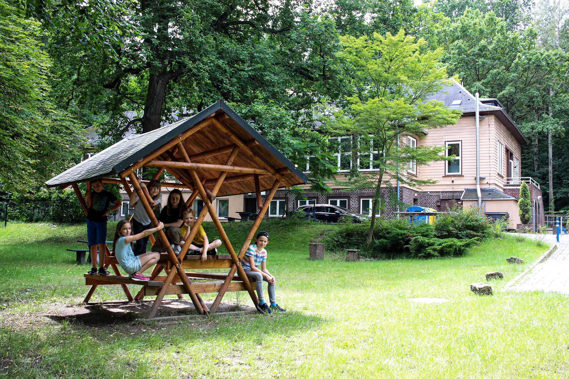 Im Vordergrund stehend eine überdachte Sitzgruppe und im Hintergrund das Haupthaus.
