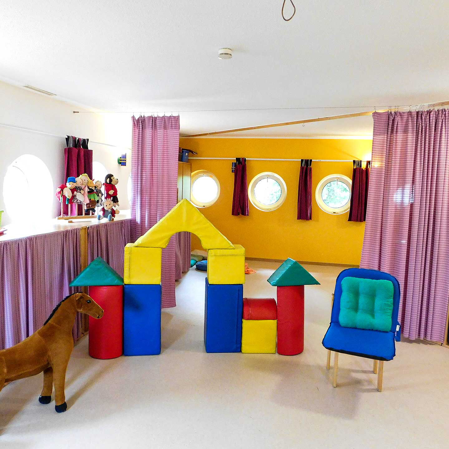 Im Spielzimmer steht ein Plüschpferd, ein Puppentheater und Schlafmatten im Regal.