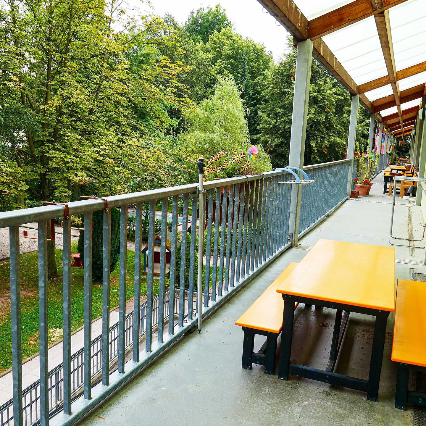 Ein Blick von der Rampe in Richtung des Gartens. Auf der Rampe steht ein Tisch mit zwei Bänken und im Garten sind diverse Spielgeräte.