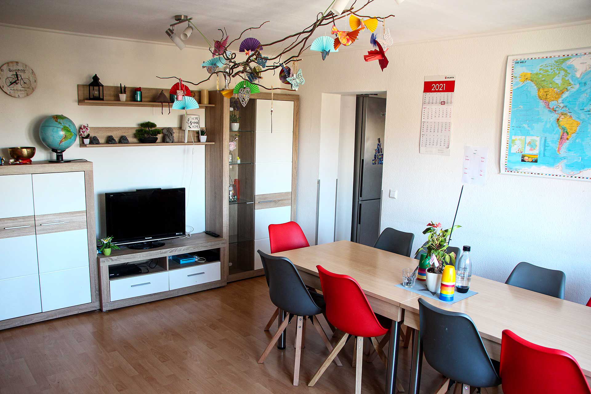 Das Gruppenzimmer mit zwei Tischen mit Stühlen, einer Anbauwand und TV.