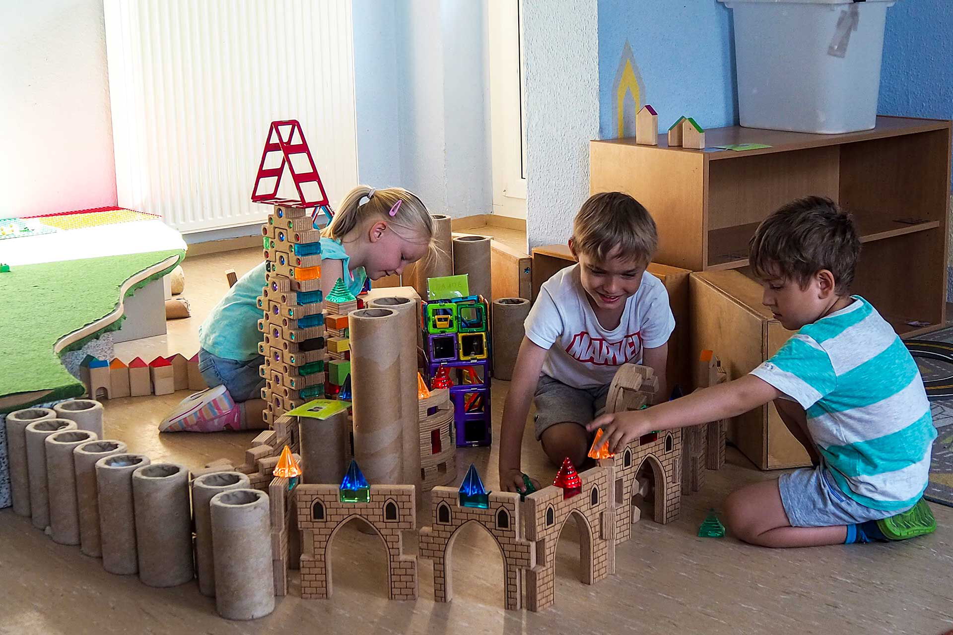 Bauzimmer Im Bauzimmer spielen drei Kinder mit Bausteinen und haben viele Türme und Zäune aufgebaut.