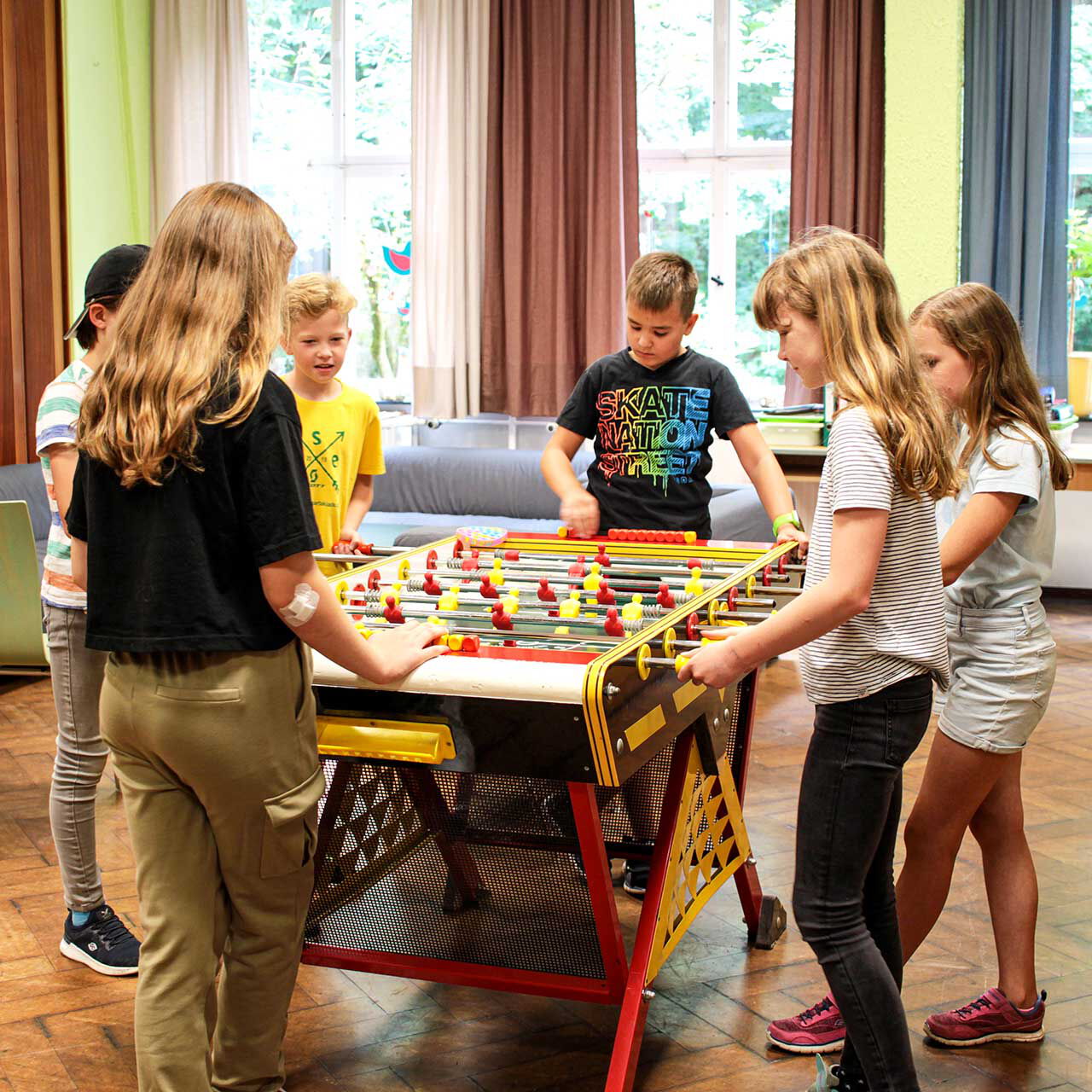 Im Veranstaltungssaal spielen sechs Kinder gemeinsam an einem Kickertisch.