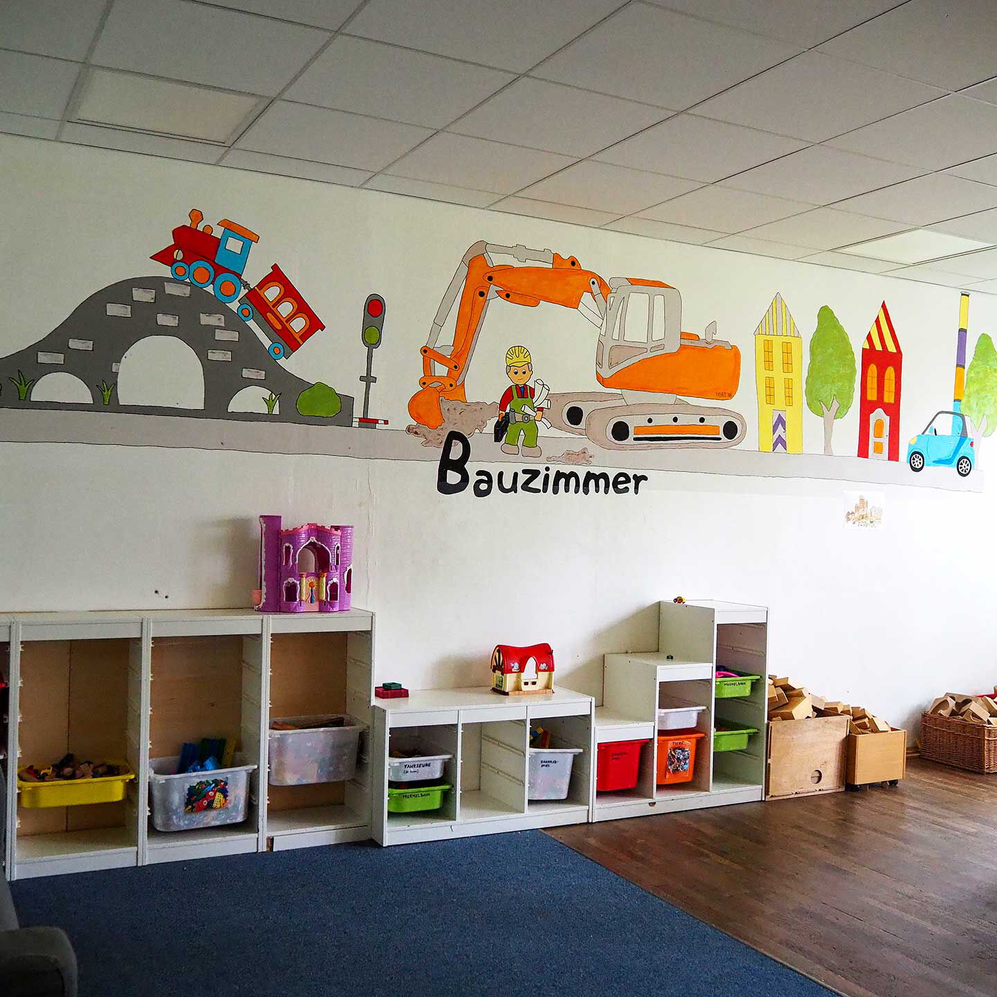 Im Bauzimmer sind mehrere Regale mit Baumaterial, ein großer Teppich und Holzbausteine.