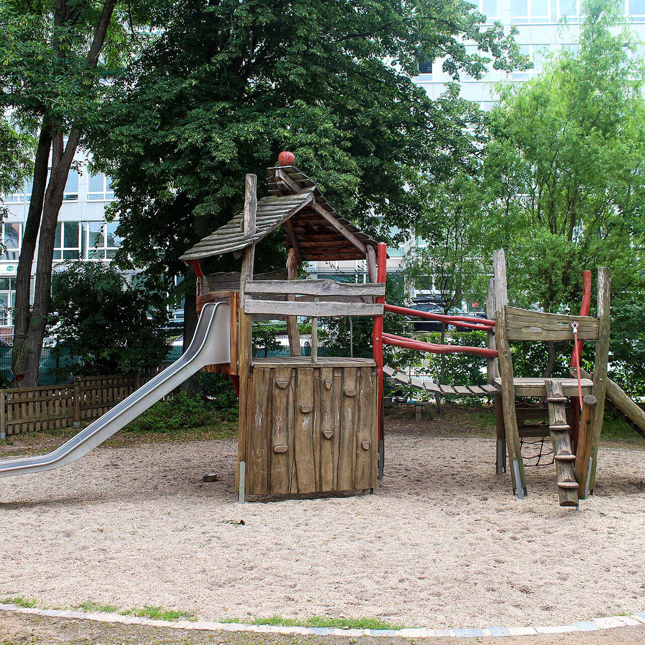 Ein Spielturm aus Holz mit einer Rutsche und Klettergerüst im Außengelände.