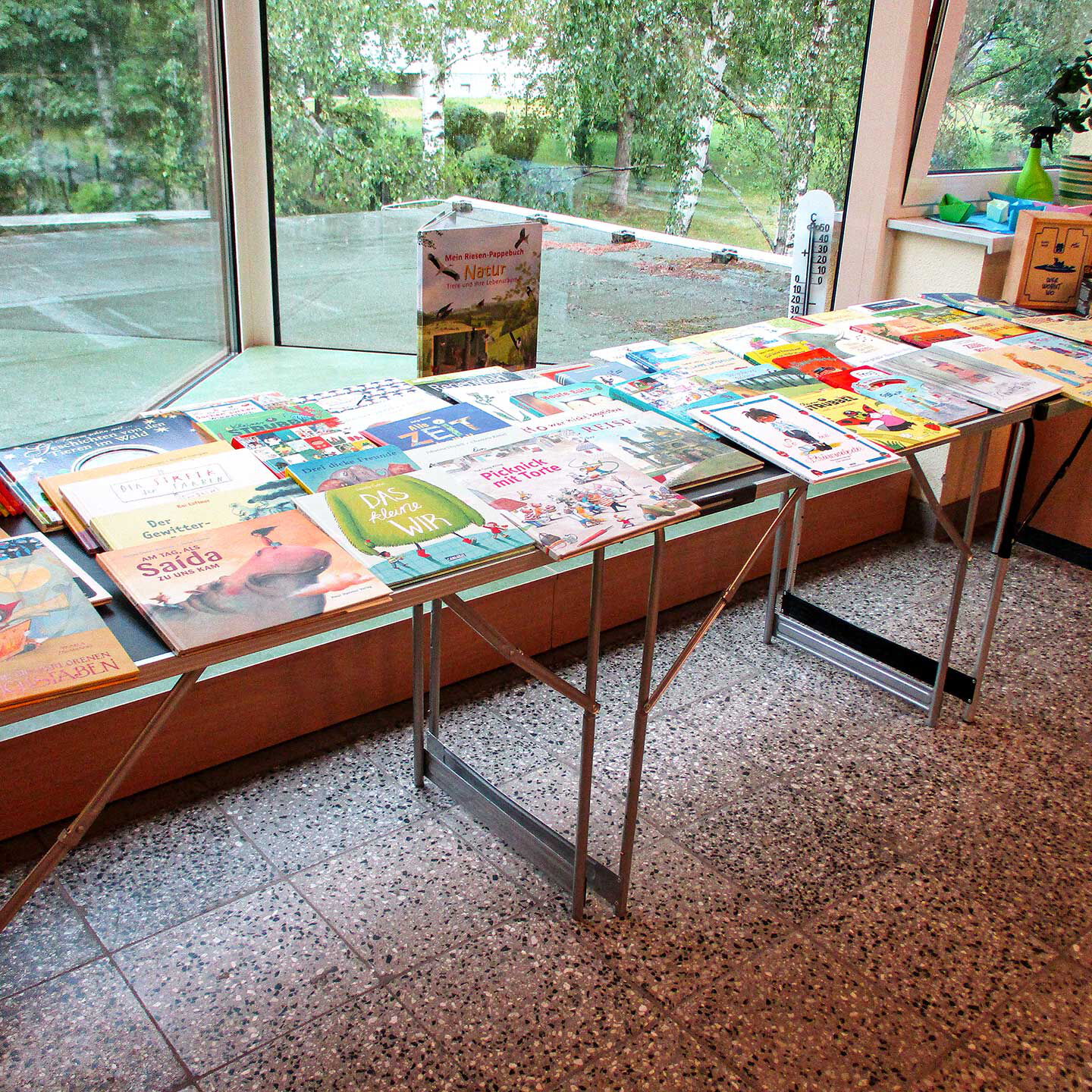 Mehrere Tische und Bänke auf denen Bücher und Spiele liegen. Einmal monatlich können sich Familien Bücher und Spiele in unserer Mediathek ausleihen und in Ruhe zuhause lesen oder ausprobieren.
