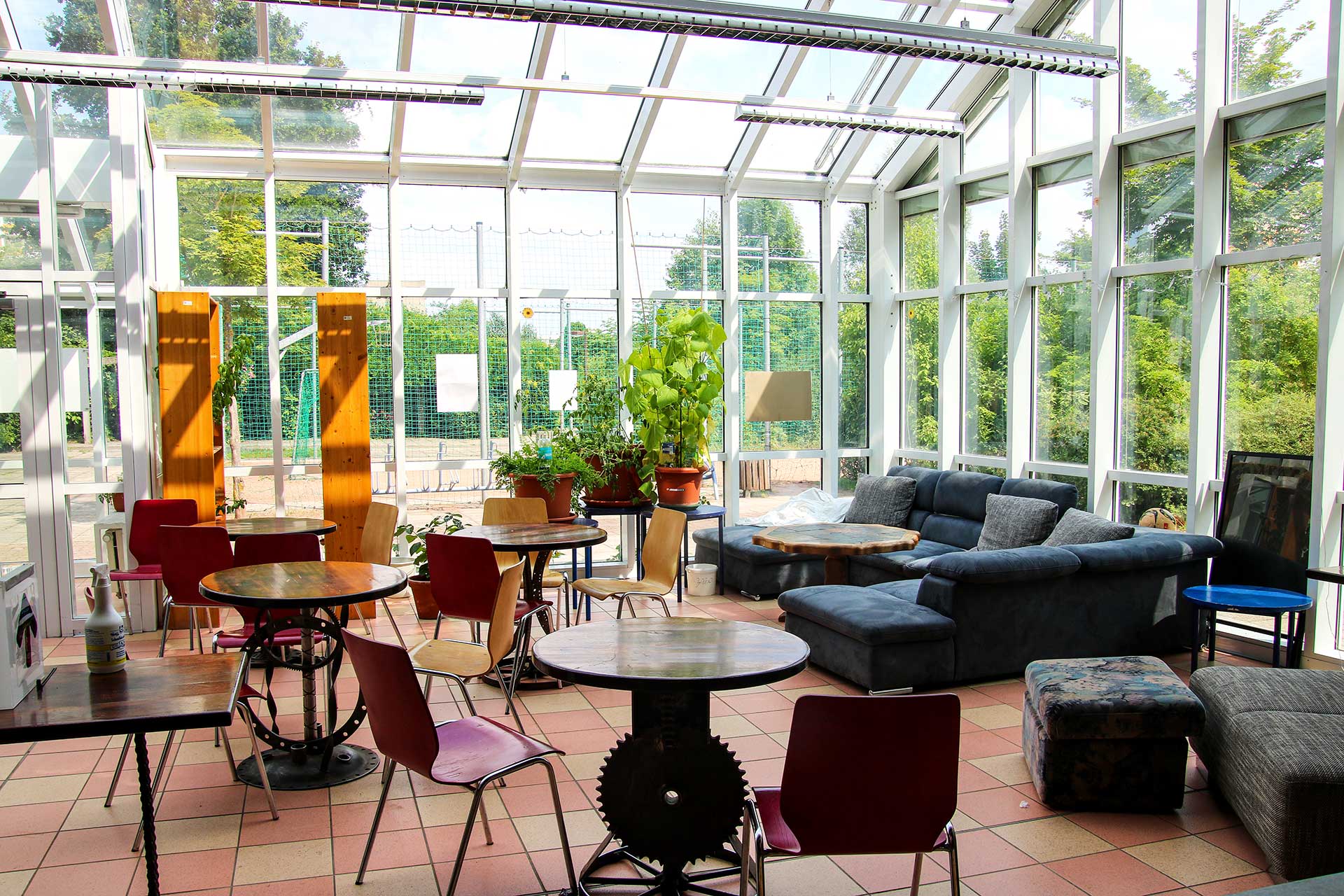 unterer Sitzbereich Der Sitzbereich im Erdgeschoss mit einer großen Couch und vier kleinen Tischen mit jeweils zwei Stühlen Die Überdachung ist ein Wintergarten.
